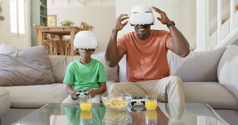 African American Father and Son Playing Virtual Reality Games on Cozy Beige Sofa at Home