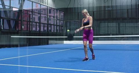 Female athlete playing paddle tennis on indoor court in activewear