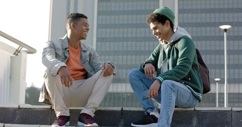 African american friends sitting on urban ledge chatting with smartphone and backpack