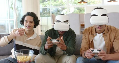 Friends enjoying VR gaming on couch eating chips together in modern living room