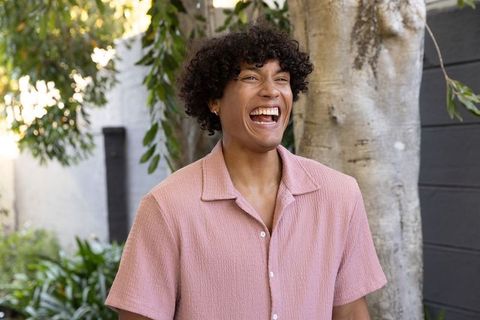 Man laughing and standing in sunlit backyard wearing pink textured shirt