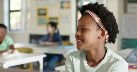 Smiling student listening in classroom wearing headband, bright daylight learning