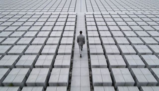 Businessman walking along symmetrical concrete grid leading lines minimalist urban concept