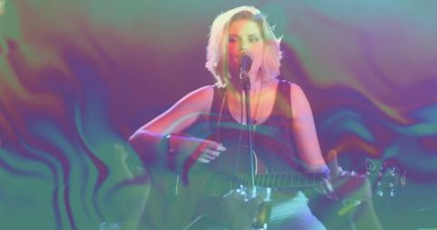 Teen musician strumming guitar on stage under colorful lights