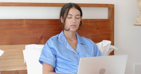 Woman in Satin Pajamas Working on Laptop in Minimalist Bedroom