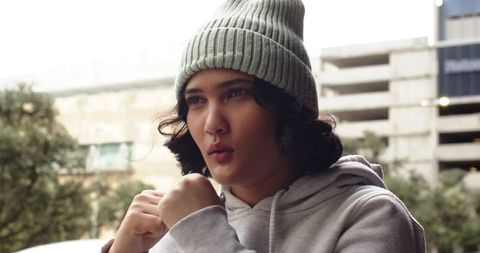 Young woman training outdoors in hoodie and beanie with fists raised and focused urban overcast back