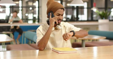 African american man checking smartwatch while calling in modern coworking cafe wearing beanie