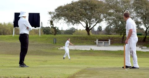 Men engaged in vigorous cricket match on green field