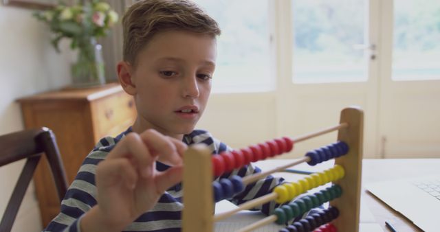Young boy uses abacus for math education at home. Ideal for educational websites, homeschooling resources, or materials promoting traditional learning methods.