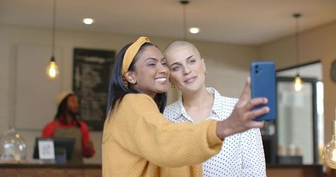 Mixed-race friends taking selfie in cozy cafe with mustard sweater and warm lighting