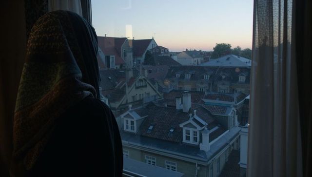 Standing woman wearing patterned scarf gazing out over historic tiled rooftops at dusk