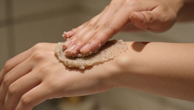Closeup hands exfoliating with granular scrub on back of hand for skincare and spa wellness