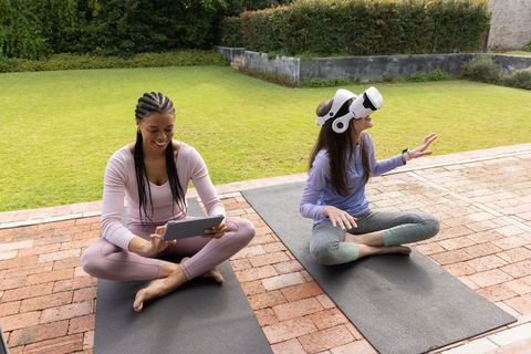 Black woman and friend practicing yoga and exploring virtual reality on backyard mats