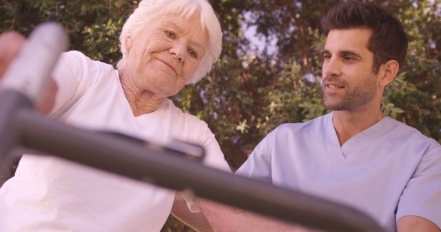 Elderly woman is receiving care and support from a young healthcare worker in an outdoor garden setting. The scene depicts compassion and attentive caregiving. Perfect for illustrating themes related to senior care, healthcare services, nursing, medical assistance, and outdoor therapy. Useful for articles, blogs, websites, and promotional materials focusing on elderly care, wellness, and support programs.