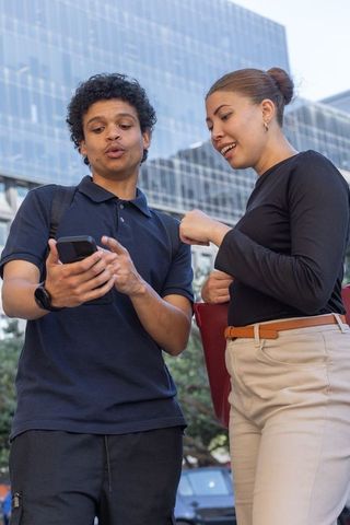 African american young professionals sharing smartphone on downtown sidewalk for teamwork
