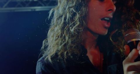 Curly-haired singer performing with wired microphone under moody blue-red stage lighting