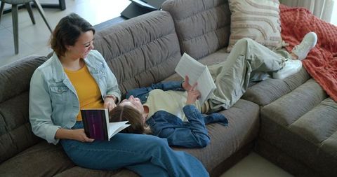Two women relaxing on sectional sofa reading paperbacks in casual denim jackets