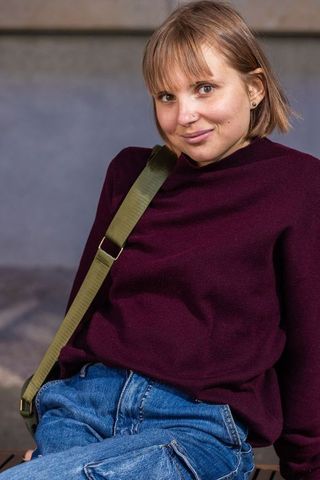 Confident young woman leaning forward in burgundy sweater with olive crossbody strap