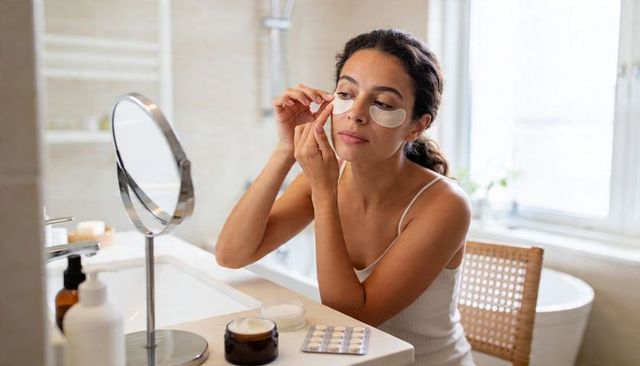 Applying under-eye patches at bathroom vanity woman practicing morning skincare routine