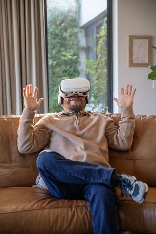 Relaxing in vr wearing headset on tan leather couch near window
