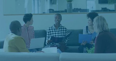 Team Collaboration in Modern Office Lounge Setting with Laptops and Folders