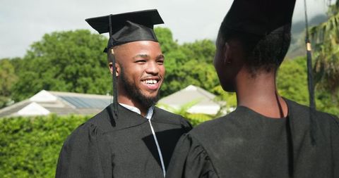 Graduating Couple Celebrating Outdoors in Caps and Gowns