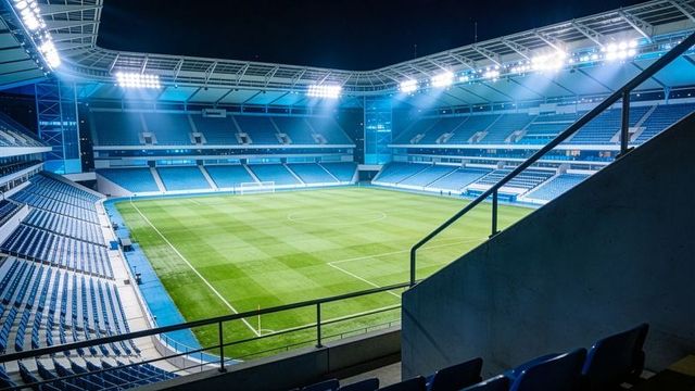 Empty modern soccer stadium glowing under floodlights at night with pristine pitch