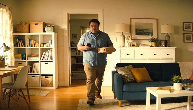 Man walking through cozy living room carrying parcel while checking smartphone, home lifestyle