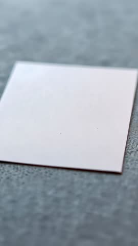 Vertical video shifting and centering white square paper on textured gray mat with subtle specks and