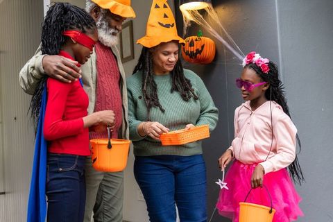 Multigenerational african american family celebrating halloween on porch in fun costumes