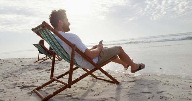 Man Relaxing on Beach Chair with Smartphone at Sandy Beach - Download Free Stock Images Pikwizard.com