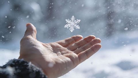 Outstretched hand catching crystal snowflake in gentle falling snow winter close-up