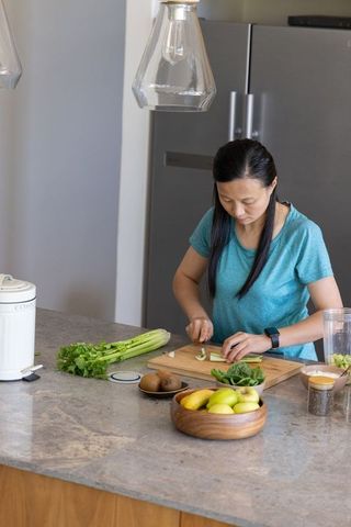 Asian woman chopping celery on kitchen countertop preparing healthy smoothie and meal prep