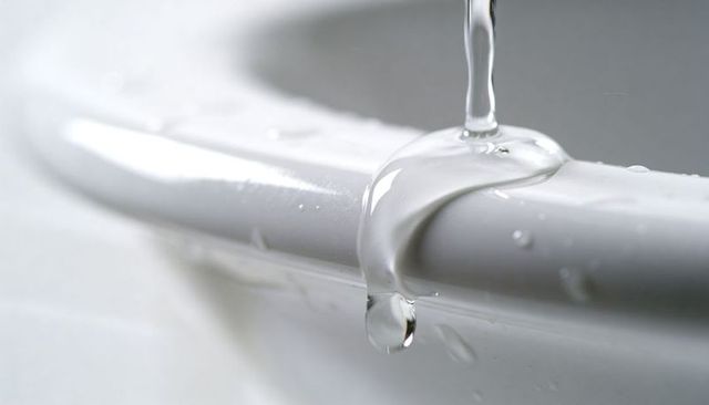 Clinging water droplet on glossy porcelain rim closeup macro bathtub drip