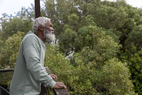 Senior african american man leaning on balcony railing overlooking green trees, quiet reflection