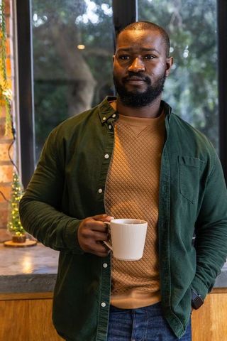 Cozy morning portrait: african american man holding white mug by window