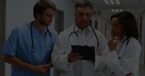 Medical Team Reviewing Patient Data on Tablet in Hospital Corridor for Clinical Collaboration