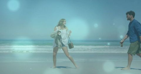 Couple walking barefoot on sunny beach holding drinks and bag for relaxed summer stroll