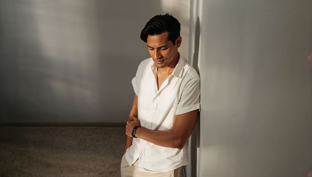 Sunlit casual man leaning against wall wearing smartwatch at golden hour