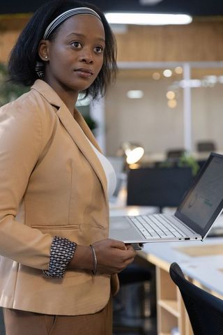 African american businesswoman holding laptop showing analytics dashboard in modern office
