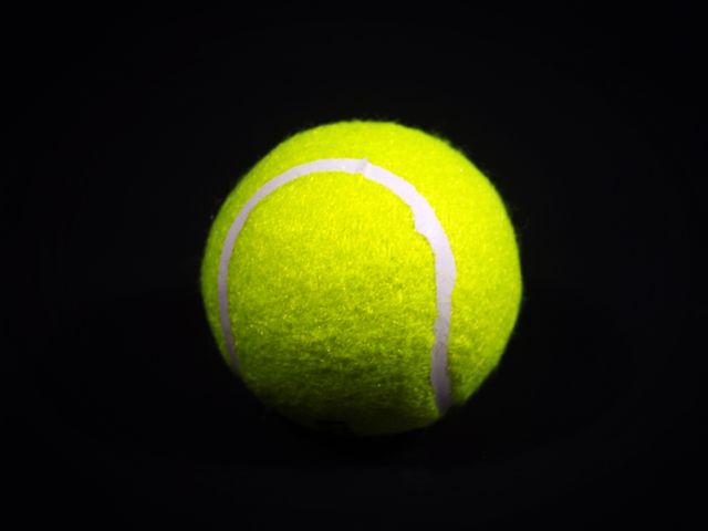 Bright yellow tennis ball against a dark black background highlighting vivid details. Ideal for sports articles, fitness blogs, product advertisements, or tennis sport promotions.
