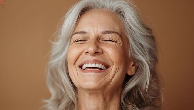Laughing mature woman with silvery hair showing joyful toothy smile and laugh lines