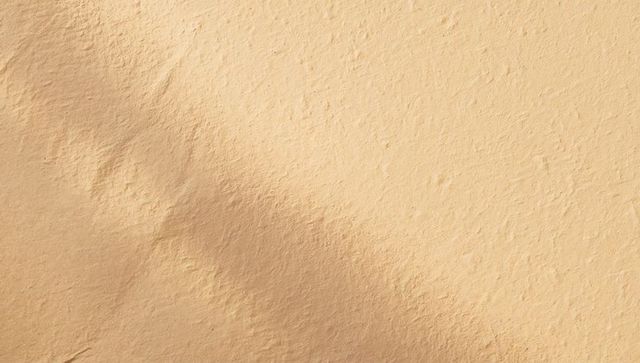 Beige textured plaster wall showing trowel marks, round dent and diagonal shade