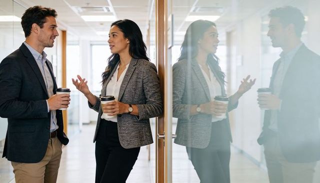 Business colleagues chatting in modern office corridor holding coffee cups and gesturing