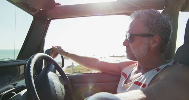 Thoughtful caucasian man in sunglasses sitting in car on sunny day by the sea. summer road trip and holiday in nature.