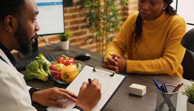 Doctor writing nutrition plan during consultation with patient and fresh produce bowl