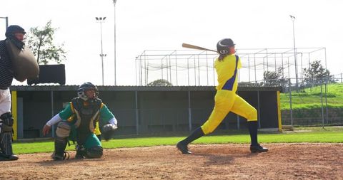 Female Softball Player Swinging Bat with Catcher and Umpire