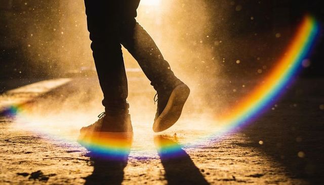Golden hour backlit steps through dust with rainbow lens flare and silhouette sneakers