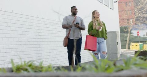 Multiracial couple walking downtown holding red shopping bag and checking smartphone