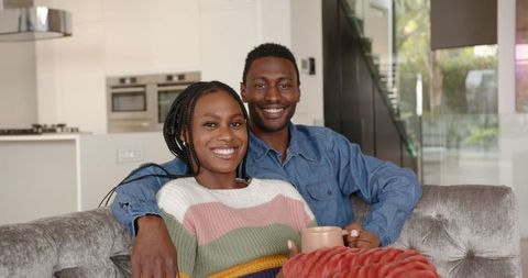 Happy Couple Relaxing on Cozy Sofa Holding Coffee Mugs
